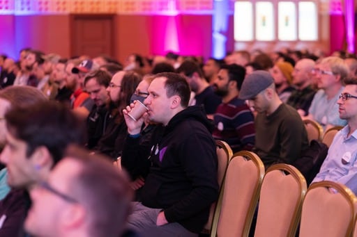 The audience, one man drinking coffee from a paper cup